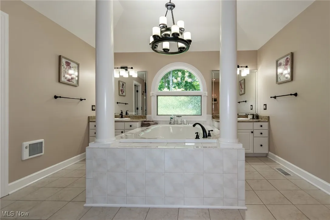 Master Bathroom with ceramic flooring, ornate columns, a jetted tub, and two vanity stations