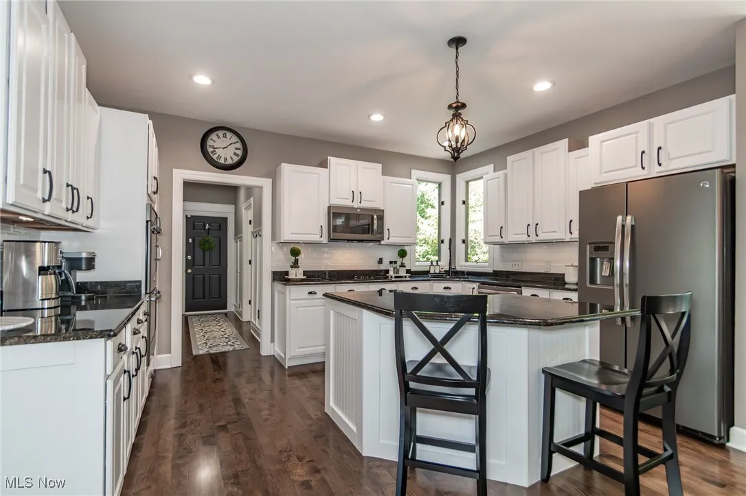 Kitchen area with center island/breakfast bar, stainless steel appliances, white cabinets, and pendulum light fixture