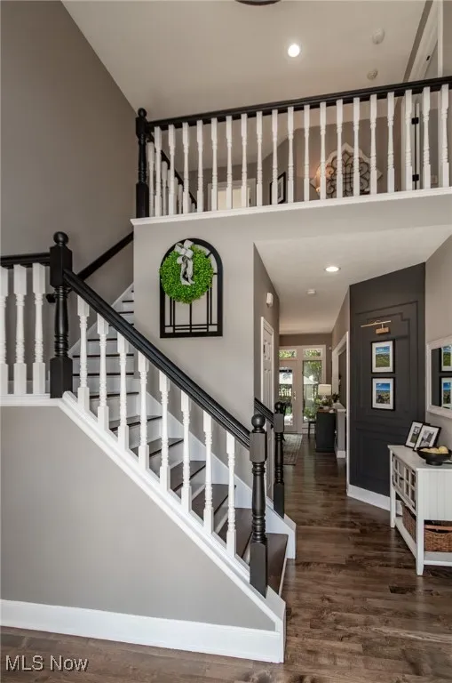 Staircase with wood finished floors, a towering ceiling, and recessed lighting