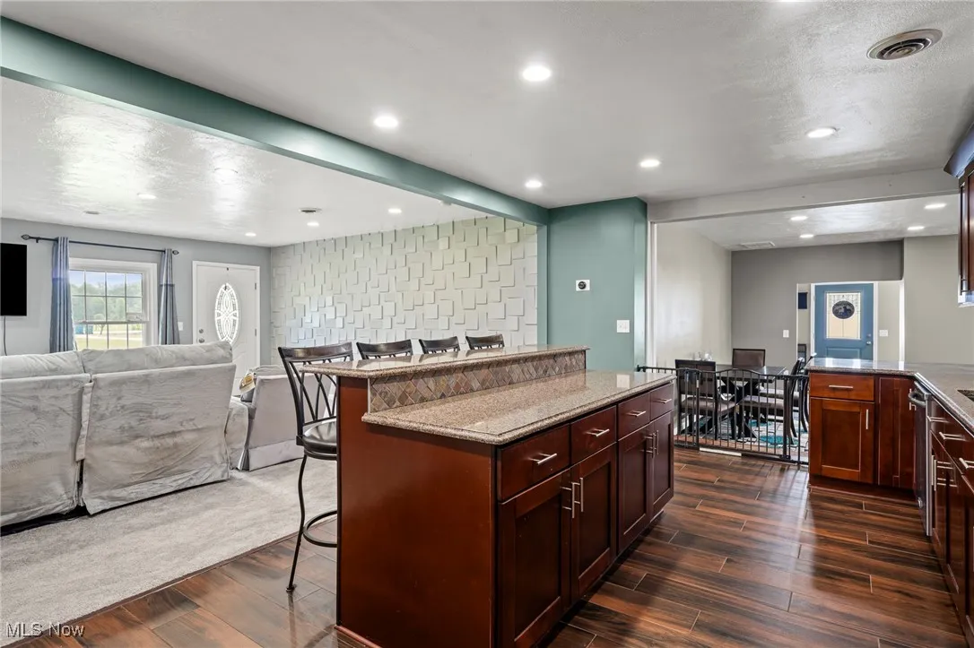 Kitchen with a kitchen bar, open floor plan, dark wood-type flooring, light stone countertops, and recessed lighting