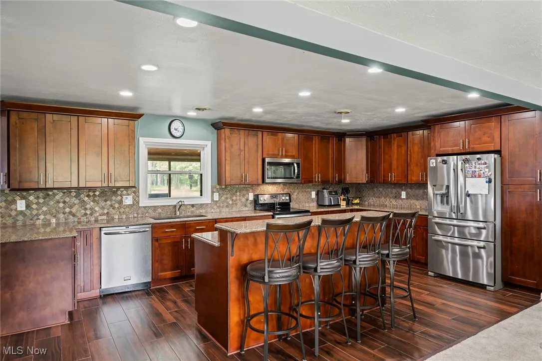 Kitchen with dark wood finished floors, stainless steel appliances, a kitchen island, recessed lighting, and a kitchen bar