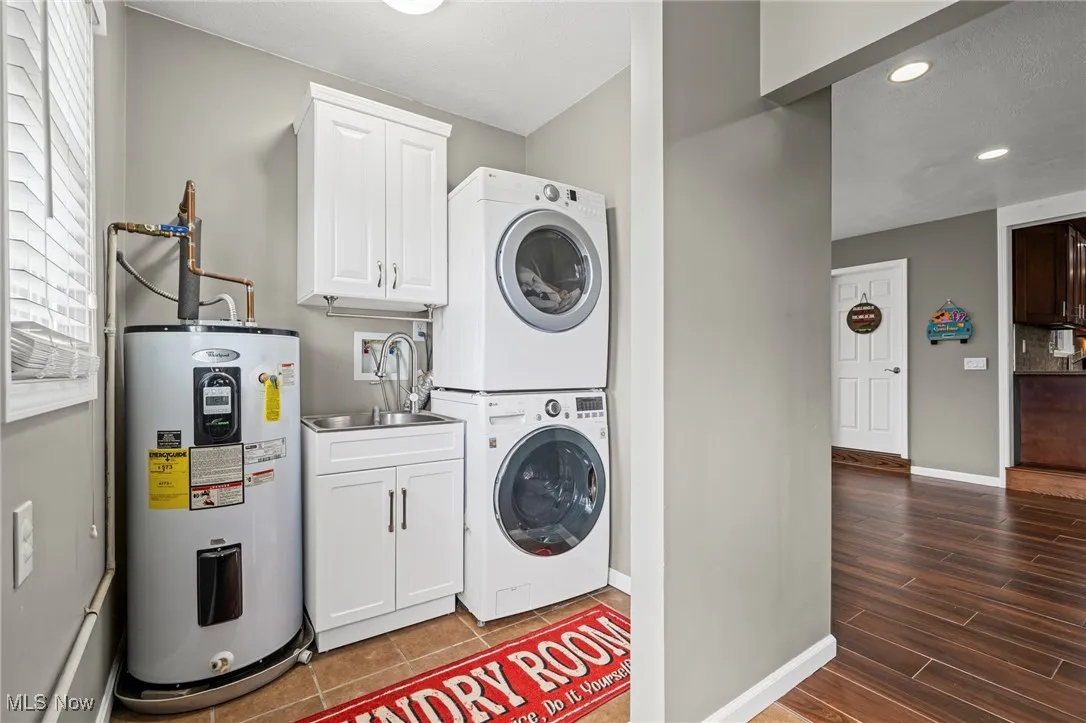 Laundry area featuring stacked washer / dryer, water heater, cabinet space, recessed lighting, utility sink, and wood finished floors