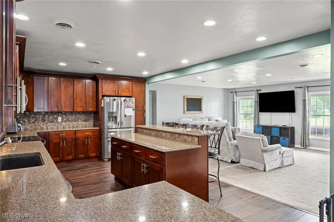Kitchen featuring open floor plan, stainless steel fridge with ice dispenser, light stone countertops, a kitchen bar, and recessed lighting