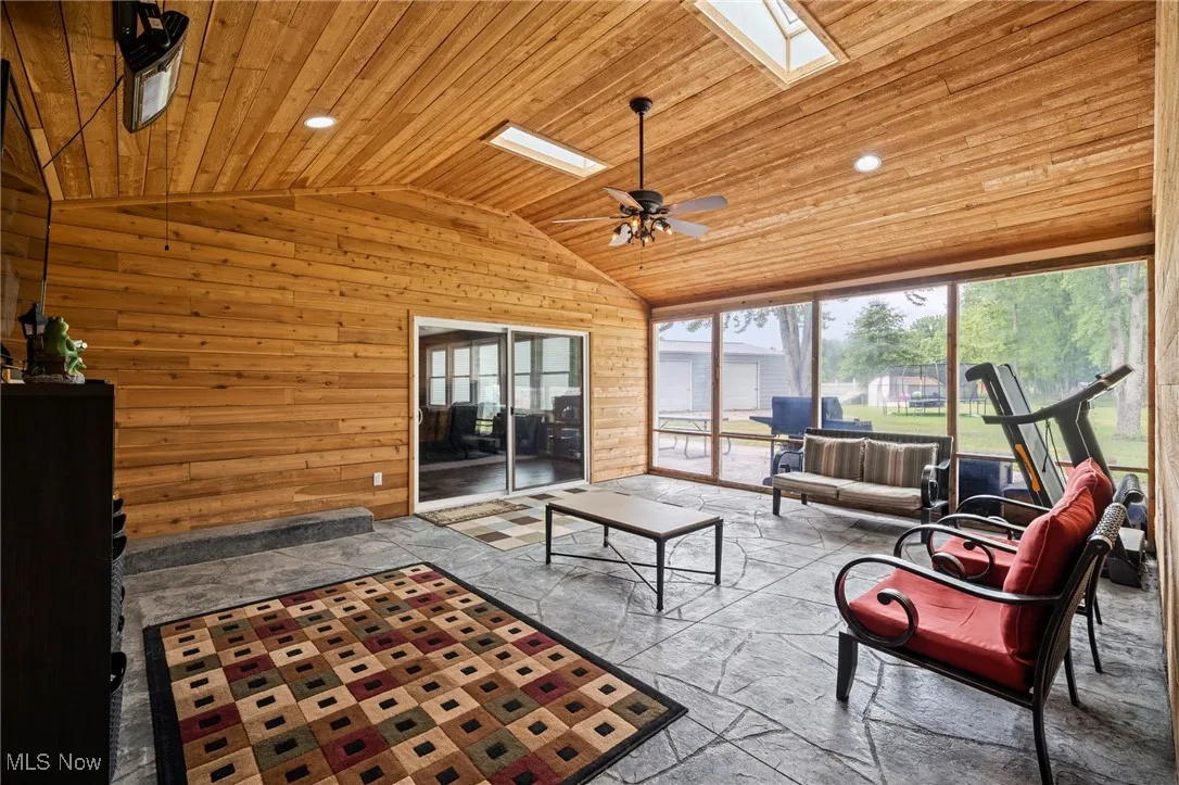 Three seasons room with wood ceiling, vaulted ceiling, a skylight, wood walls, and a ceiling fan