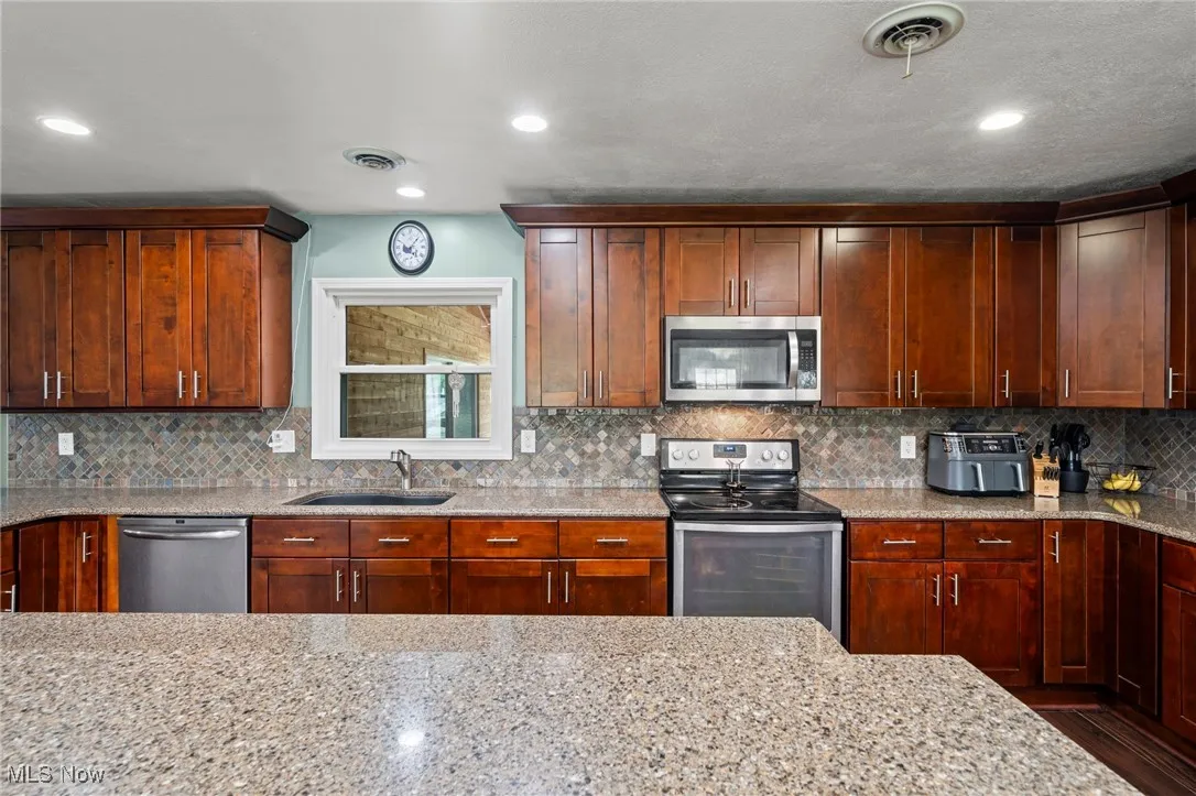 Kitchen with stainless steel appliances, light stone counters, backsplash, and recessed lighting