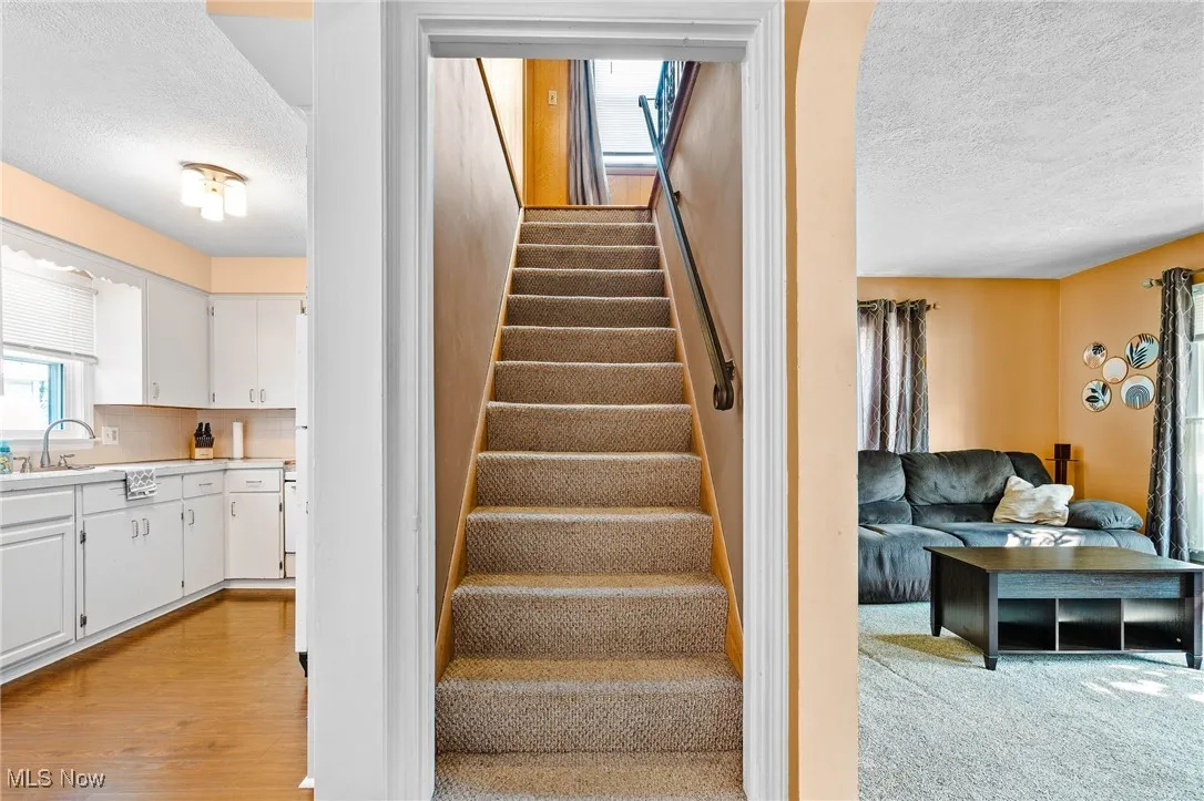 Carpeted Stairway to the 2nd floor with a view of the eat-in Kitchen and Living Room on either side of the stairwell