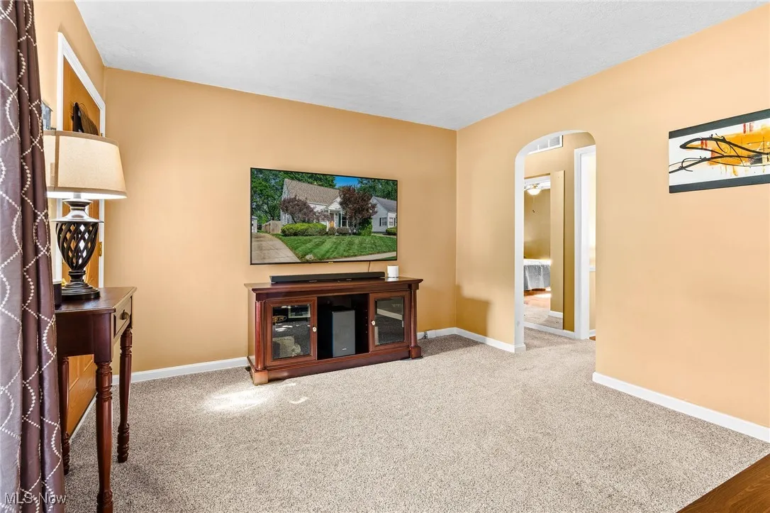 Living room with newer carpet over hardwood floors, newer windows, and an archway leading to the eat-in kitchen, two first floor bedrooms, and the updated main bath