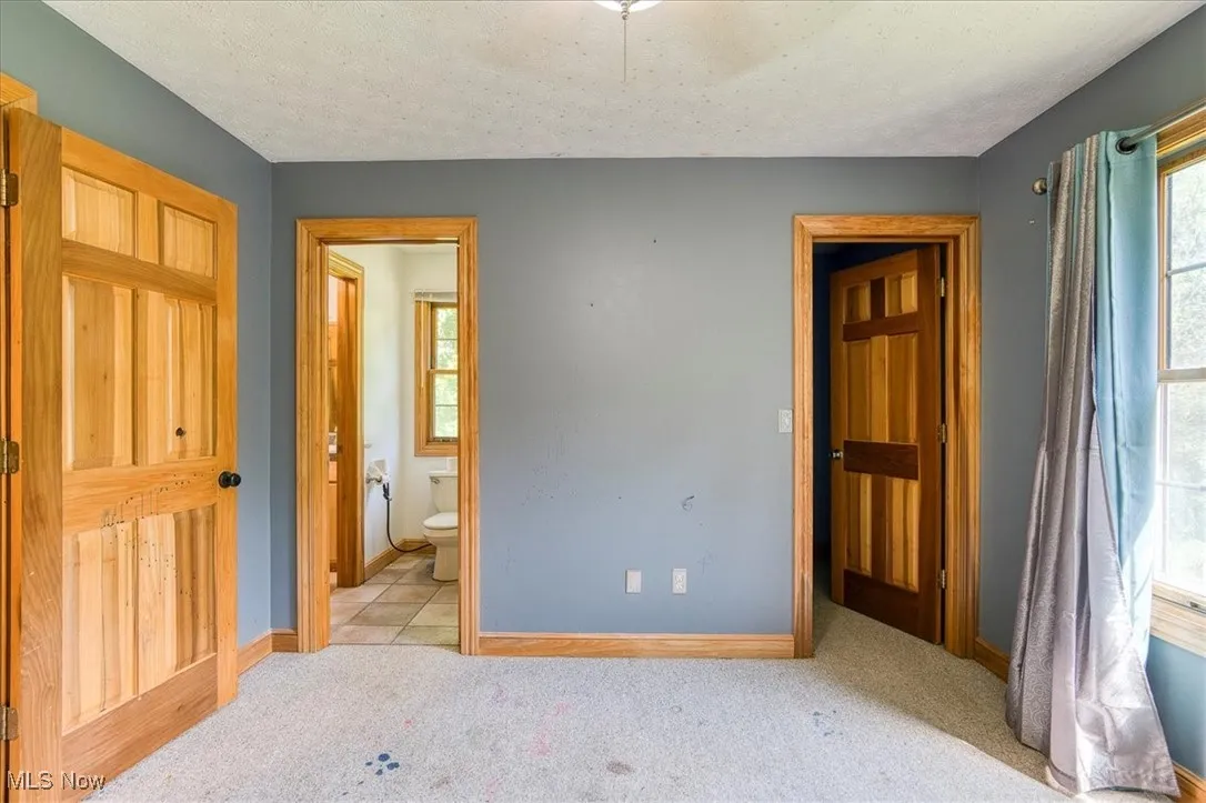 Unfurnished bedroom featuring light carpet, ensuite bathroom, and a textured ceiling