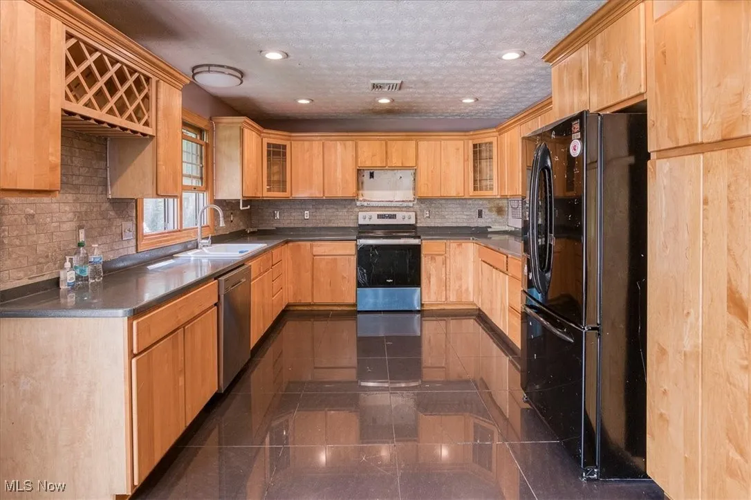 Kitchen with appliances with stainless steel finishes, recessed lighting, glass insert cabinets, backsplash, and light brown cabinets