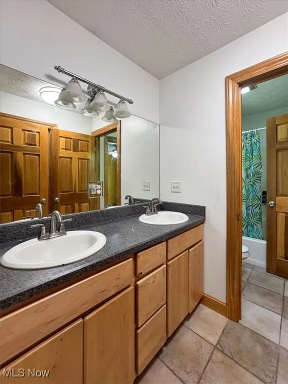 Bathroom with double vanity, a textured ceiling, and shower / tub combo