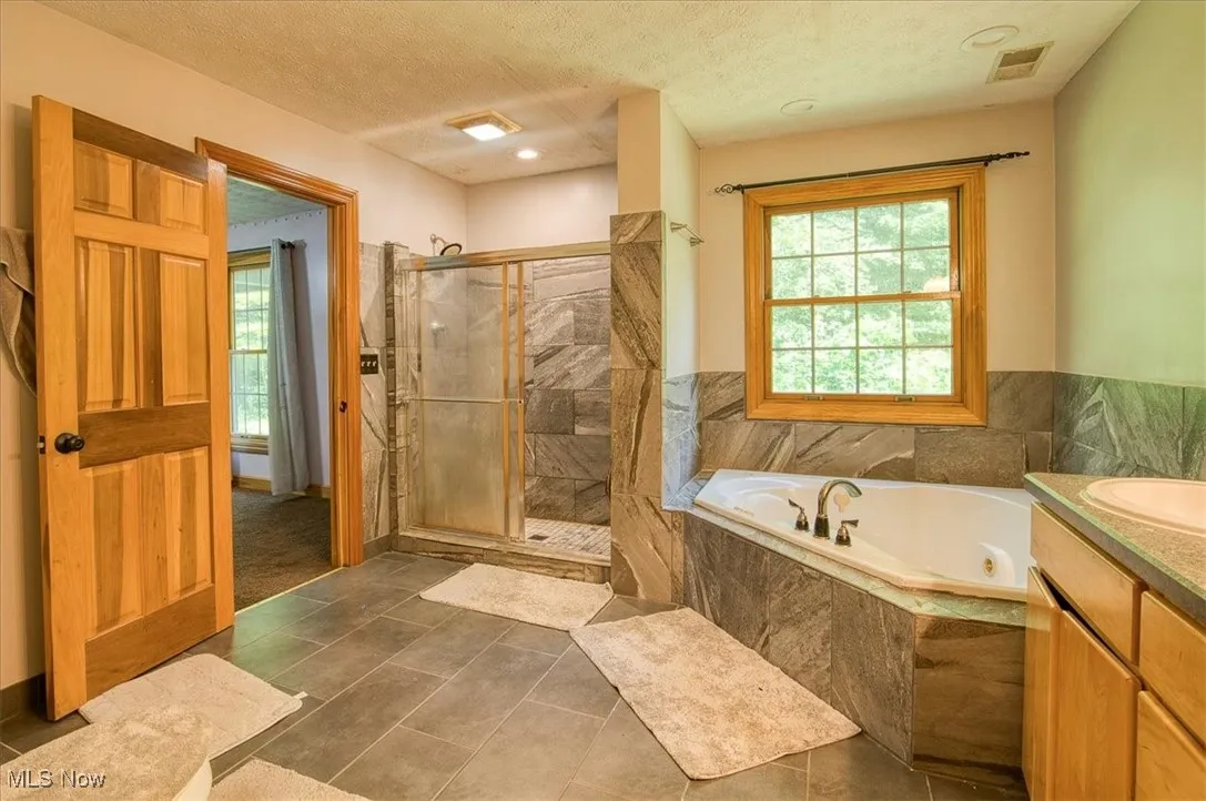 Full bathroom featuring a shower stall, a jetted tub, vanity, and tile patterned floors