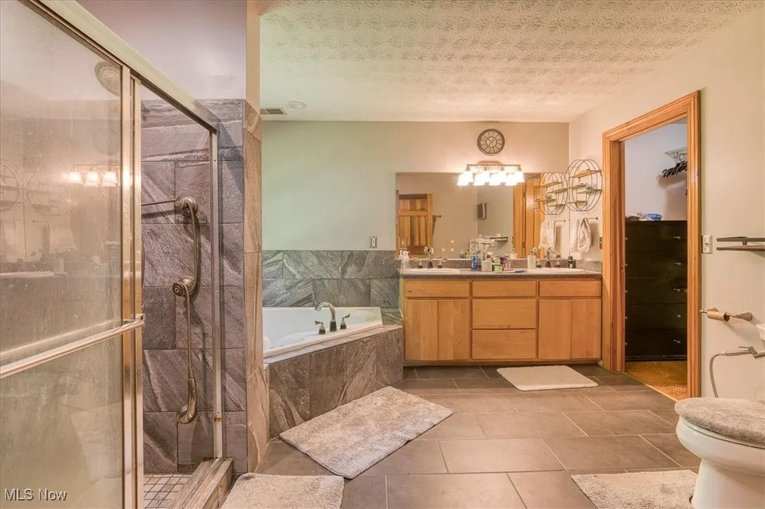 Full bath featuring vanity, tile patterned flooring, a garden tub, a shower stall, and a textured ceiling