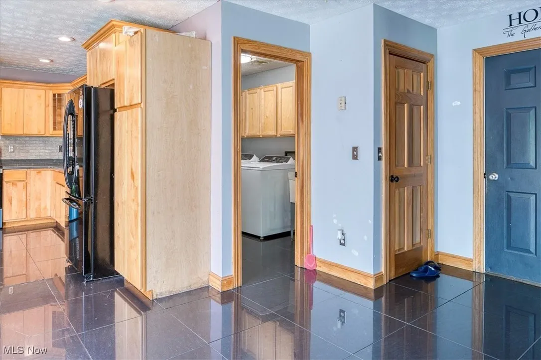 Kitchen with freestanding refrigerator, washing machine and dryer, light brown cabinets, backsplash, and a textured ceiling