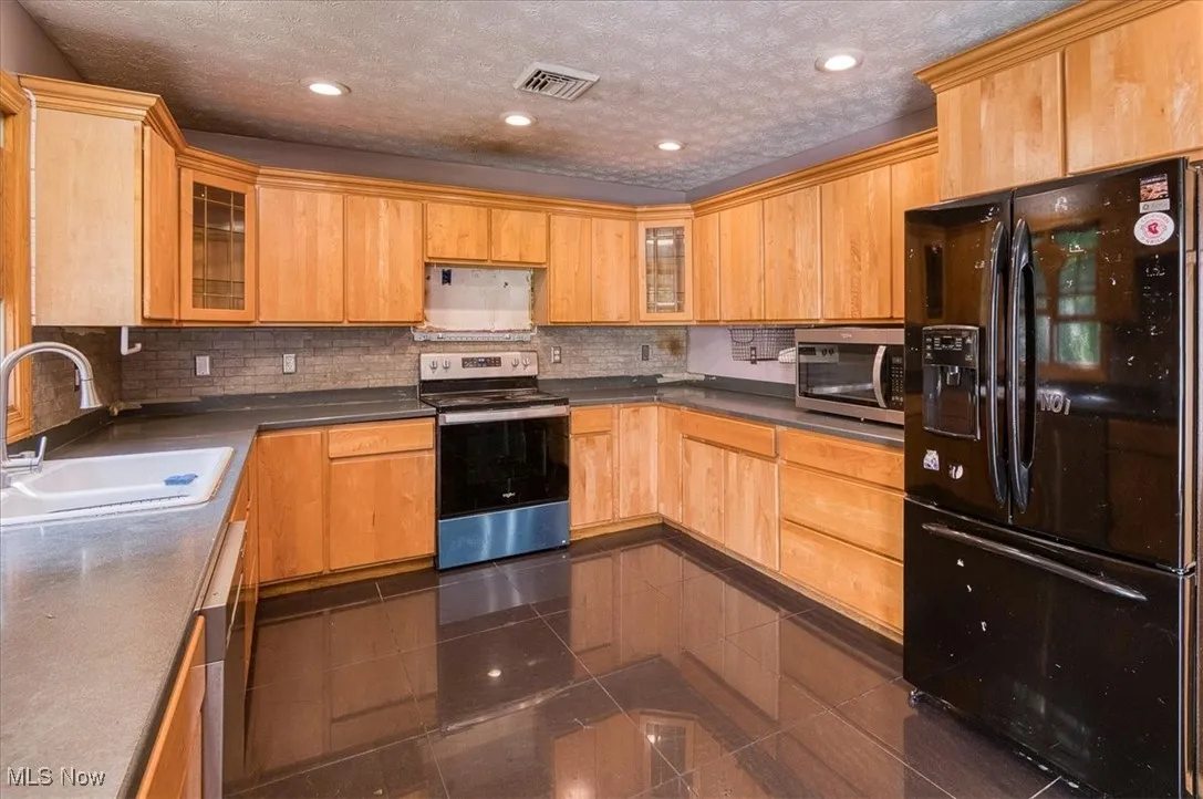 Kitchen featuring appliances with stainless steel finishes, backsplash, glass insert cabinets, recessed lighting, and a textured ceiling