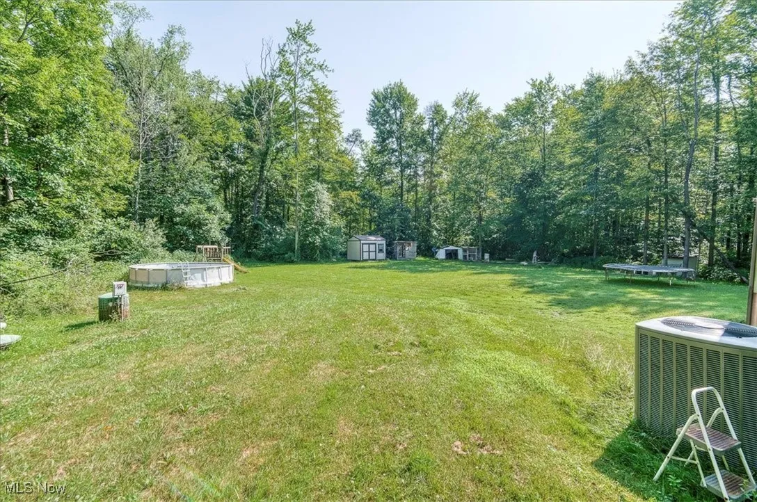 View of grassy yard featuring a trampoline, a shed, an outdoor pool, and a view of trees