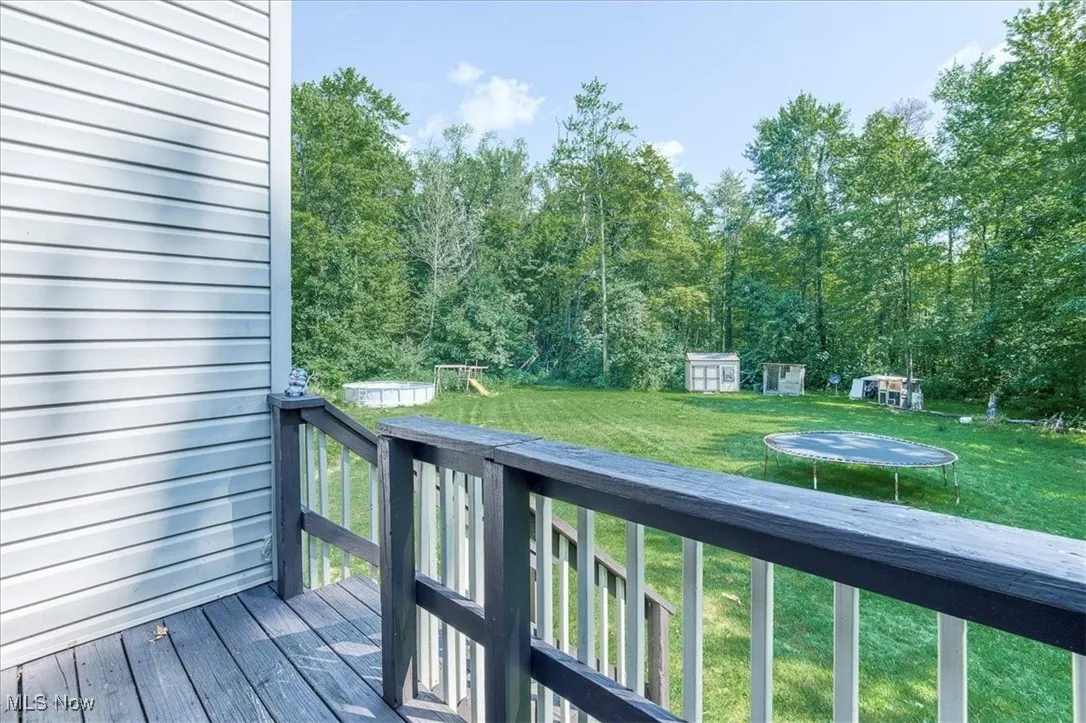 Wooden deck featuring a trampoline, a yard, a storage shed, and a forest view