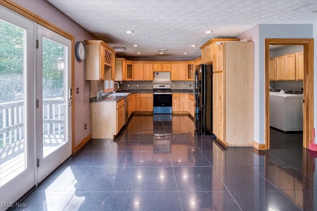 Kitchen with stainless steel electric range oven, freestanding refrigerator, white microwave, washing machine and clothes dryer, and granite floors