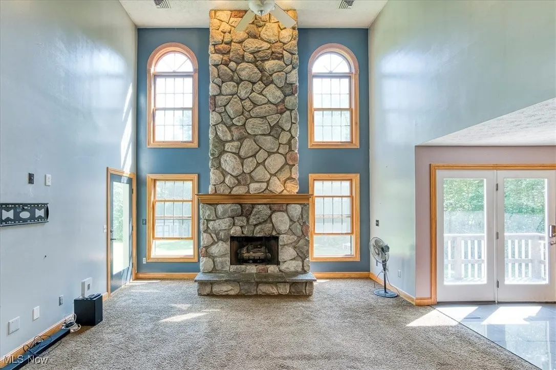 Unfurnished living room featuring plenty of natural light, carpet flooring, a high ceiling, and a fireplace
