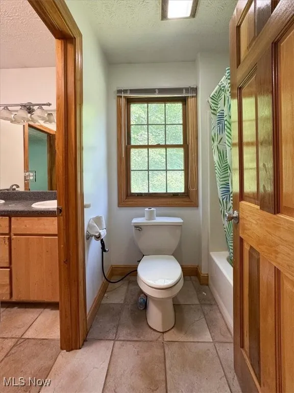 Full bath featuring a textured ceiling, vanity, and shower / tub combo with curtain