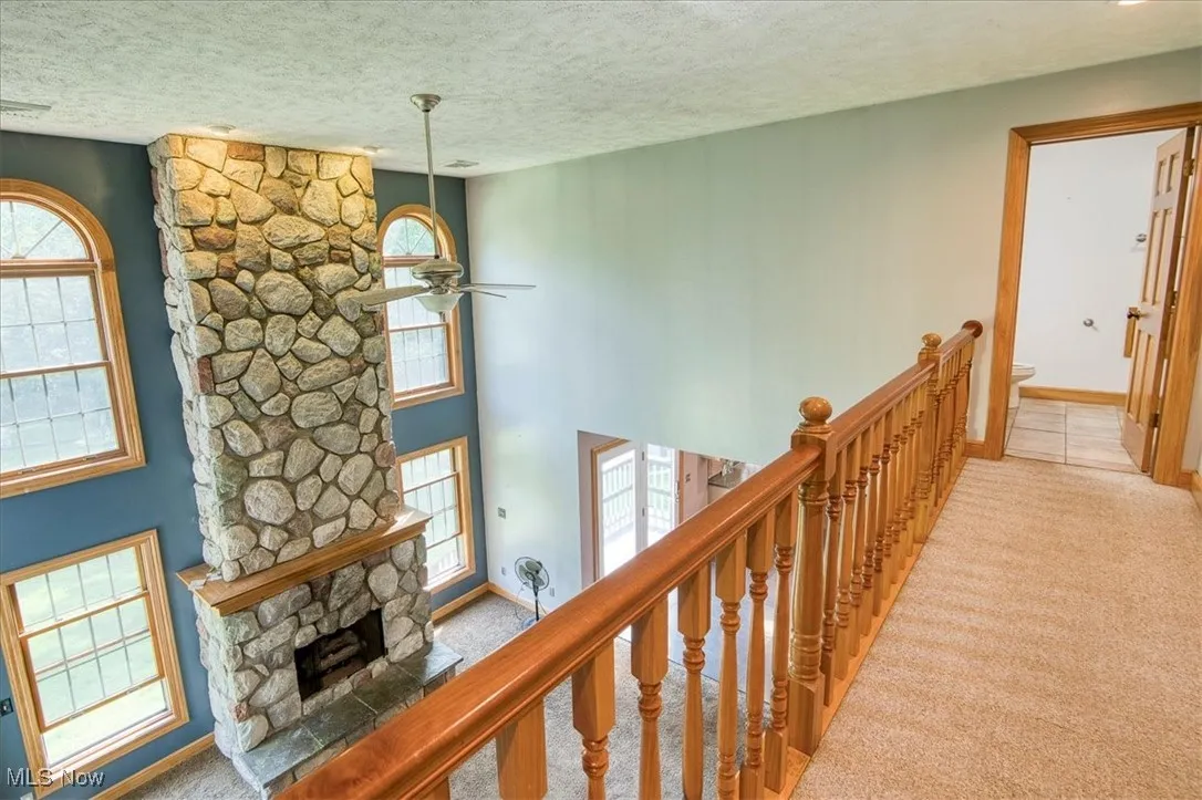 Hall with light colored carpet, a textured ceiling, and an upstairs landing