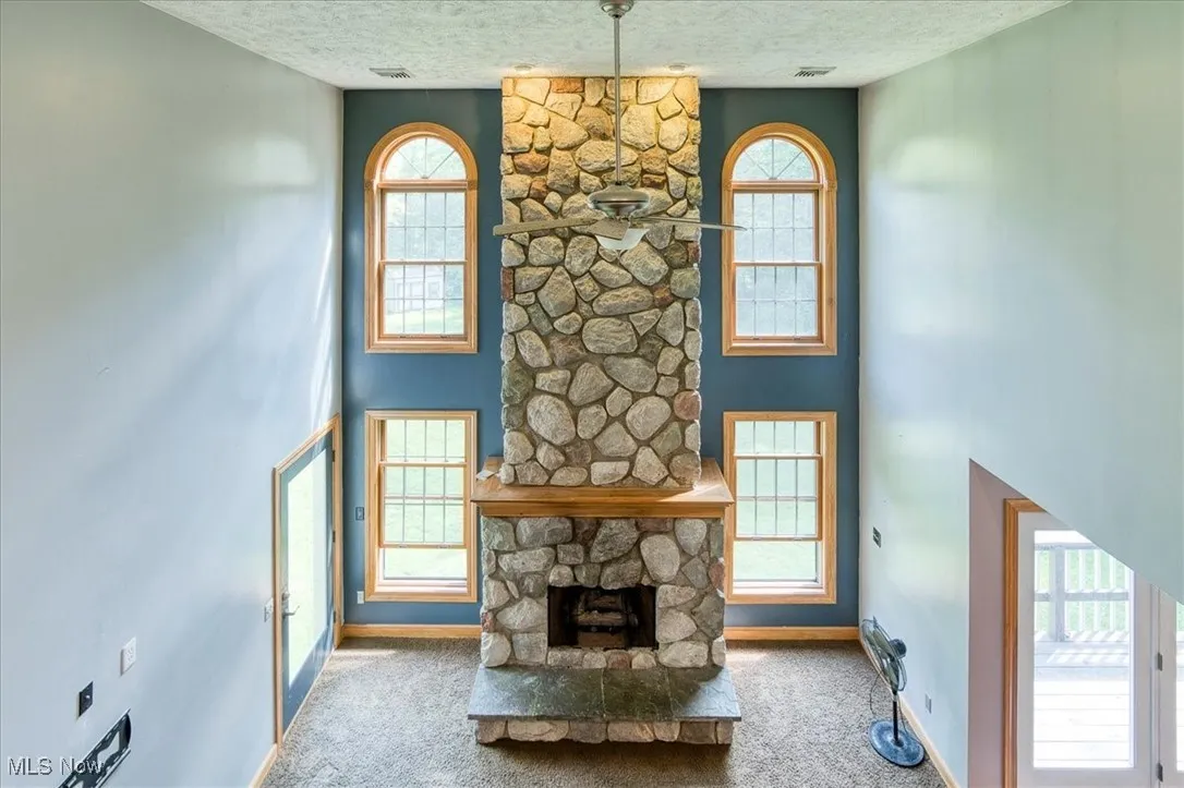 Unfurnished living room with a textured ceiling, carpet floors, a stone fireplace, and plenty of natural light