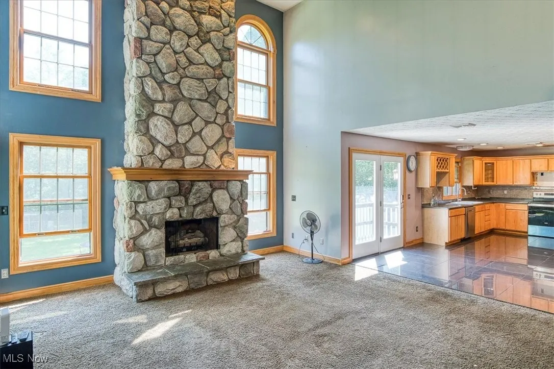 Unfurnished living room featuring plenty of natural light, a towering ceiling, dark colored carpet, and a fireplace