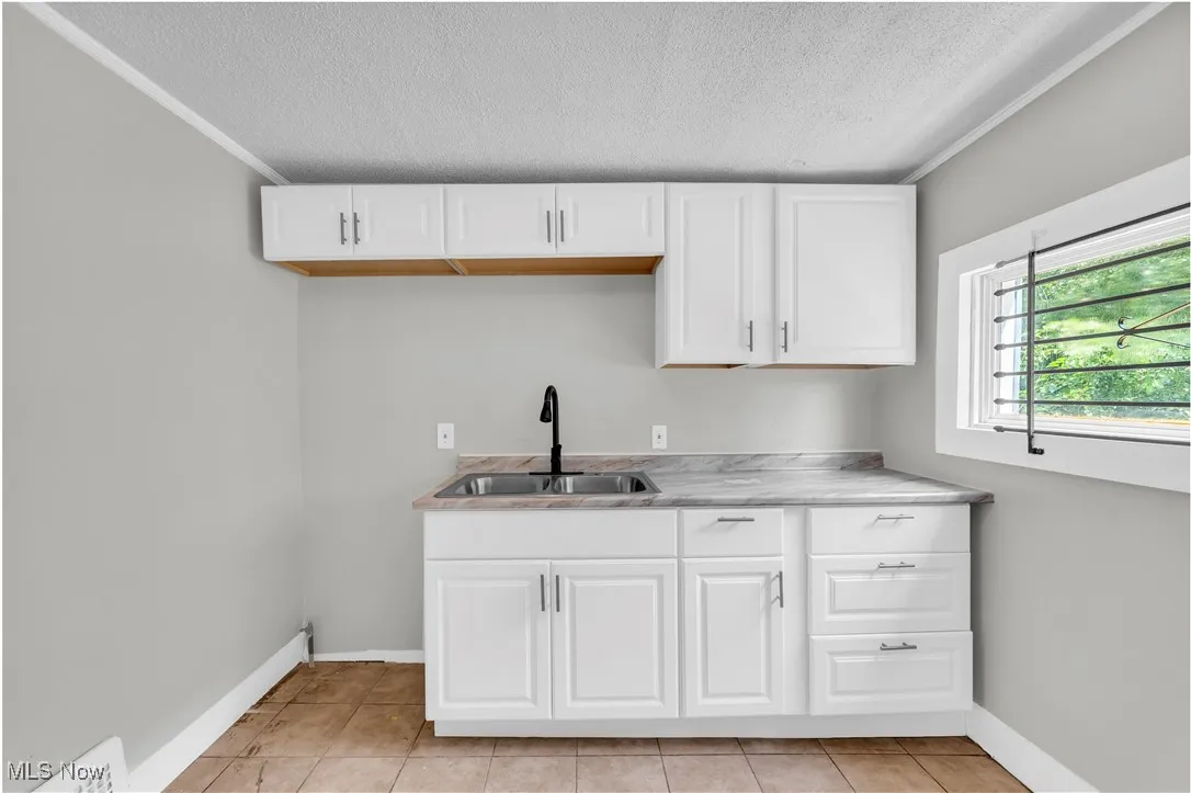 Kitchen with a textured ceiling, white cabinets, light countertops, light tile patterned flooring, and crown molding