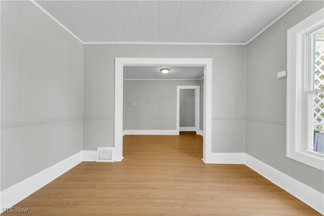 Empty room with crown molding and light wood-style floors