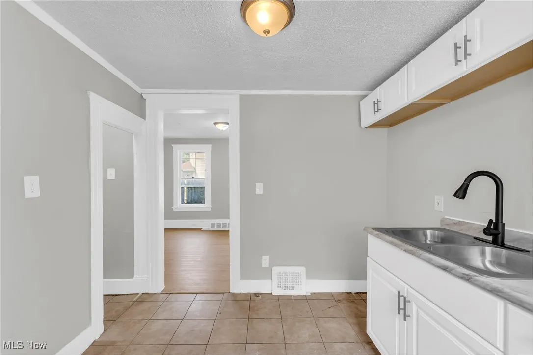 Laundry area featuring a textured ceiling, light tile patterned flooring, and crown molding