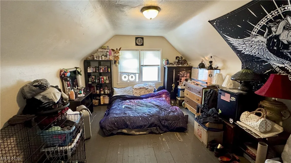 Bedroom with lofted ceiling, hardwood / wood-style floors, and a textured ceiling