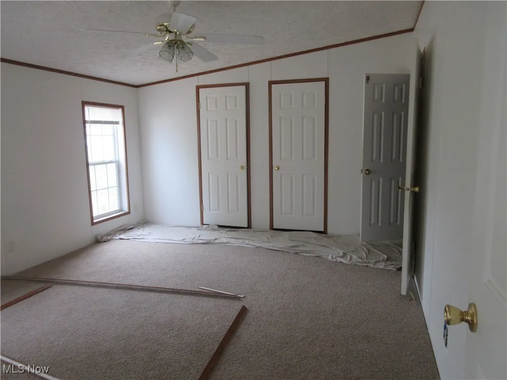 Unfurnished bedroom with ornamental molding, carpet, a textured ceiling, and a ceiling fan