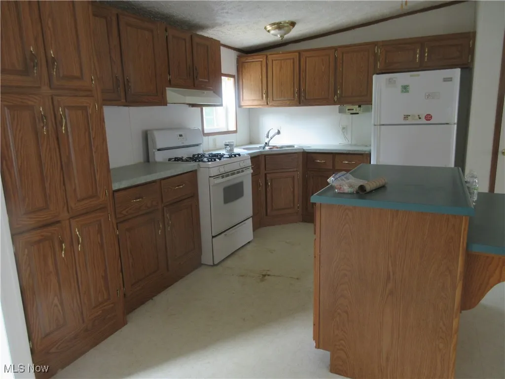 Kitchen featuring white appliances, brown cabinets, under cabinet range hood, a textured ceiling, and a center island