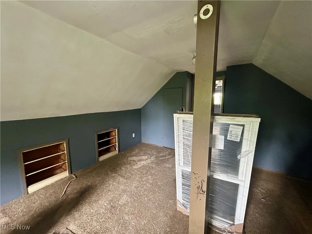 Additional living space with vaulted ceiling, built in shelves, and carpet