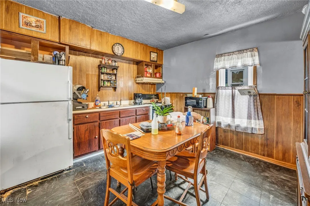 Dining room featuring wood walls, a textured ceiling, a wainscoted wall, and a baseboard heating unit