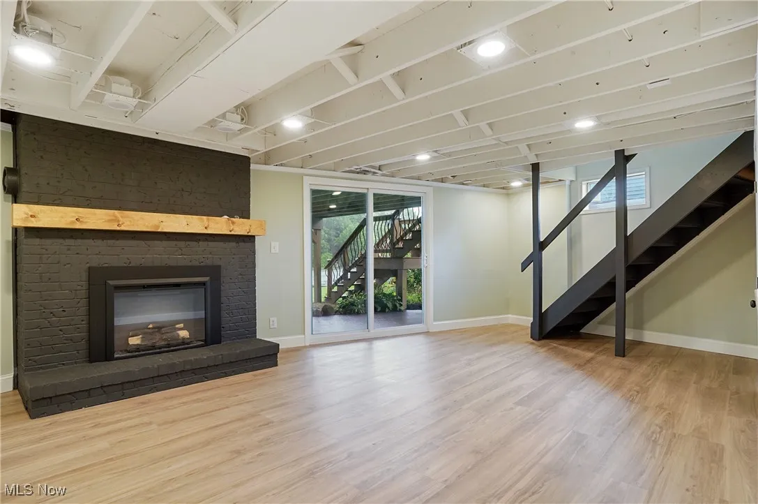 Unfurnished living room featuring stairway, wood finished floors, plenty of natural light, and a brick fireplace