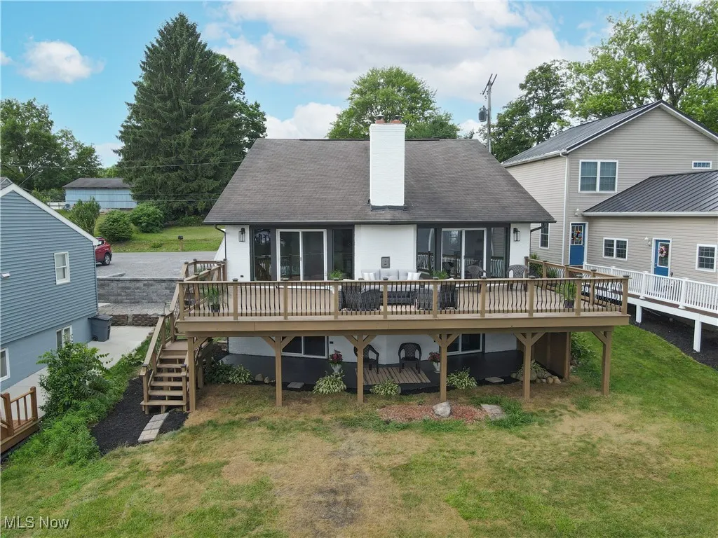 Back of house with a chimney, a deck, a lawn, stairs, and a shingled roof
