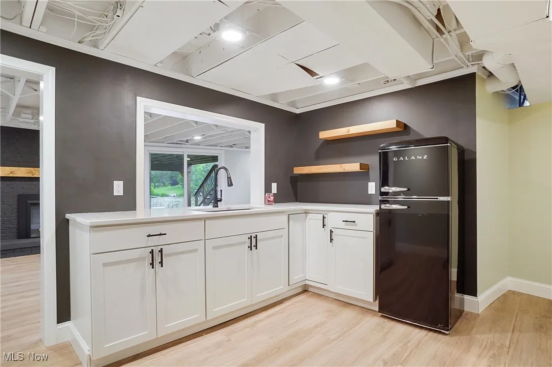 Kitchen featuring freestanding refrigerator, light wood-type flooring, white cabinets, light countertops, and a brick fireplace