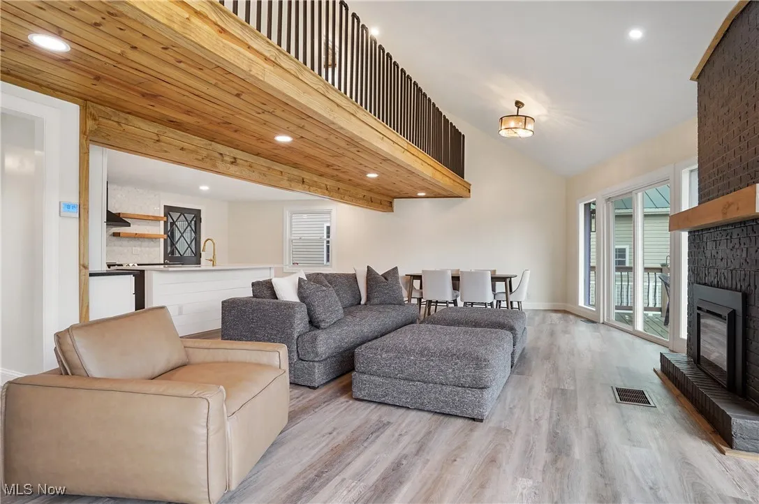 Living room with recessed lighting, light wood-style flooring, a brick fireplace, and a high ceiling