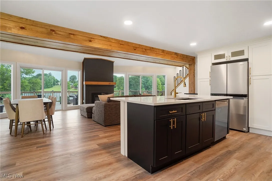 Kitchen featuring white cabinets, light countertops, appliances with stainless steel finishes, beam ceiling, and an island with sink