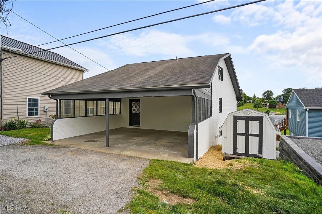 Back of property with a storage shed, an attached carport, a shingled roof, and asphalt driveway