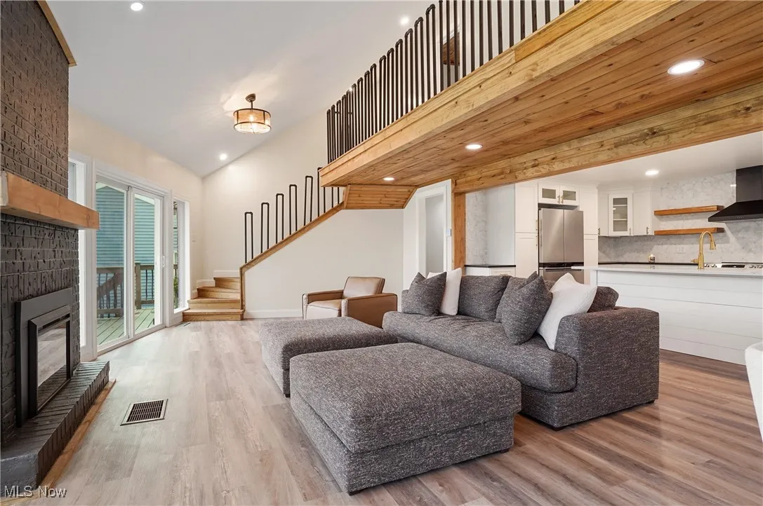 Living room with light wood-style flooring, stairs, a brick fireplace, and recessed lighting
