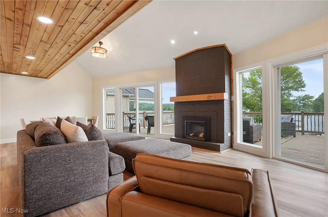 Living room featuring recessed lighting, light wood finished floors, vaulted ceiling, a brick fireplace, and wooden ceiling