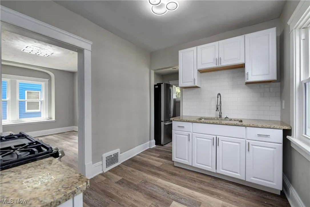 Kitchen featuring white cabinetry, decorative backsplash, freestanding refrigerator, light stone counters, and dark wood-style floors