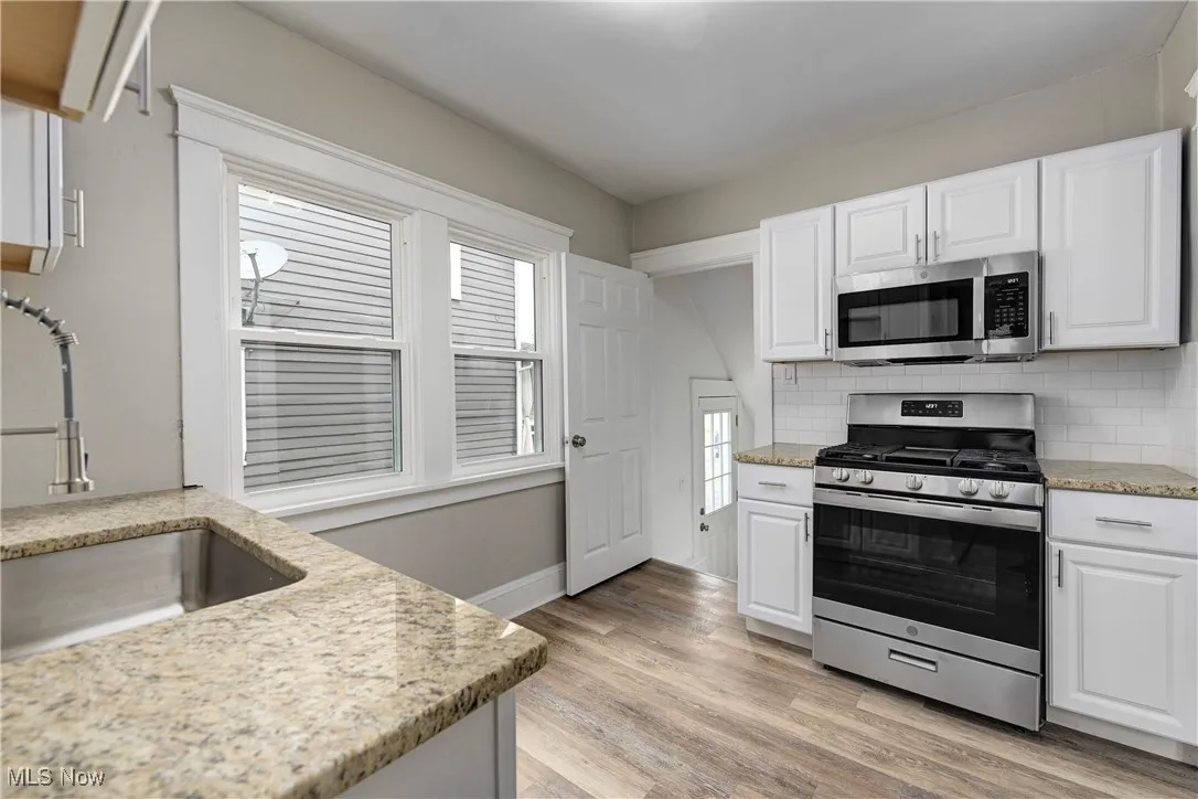 Kitchen featuring appliances with stainless steel finishes, white cabinets, decorative backsplash, and light wood-style flooring