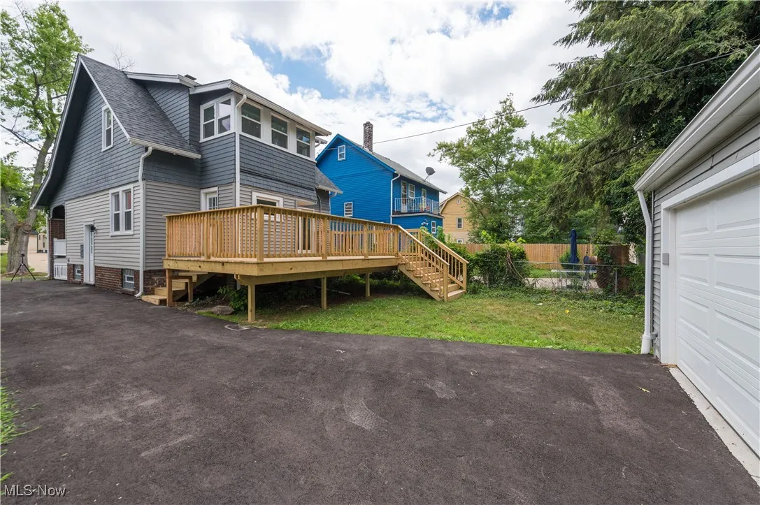 Back of property with a garage, a deck, a shingled roof, and asphalt driveway