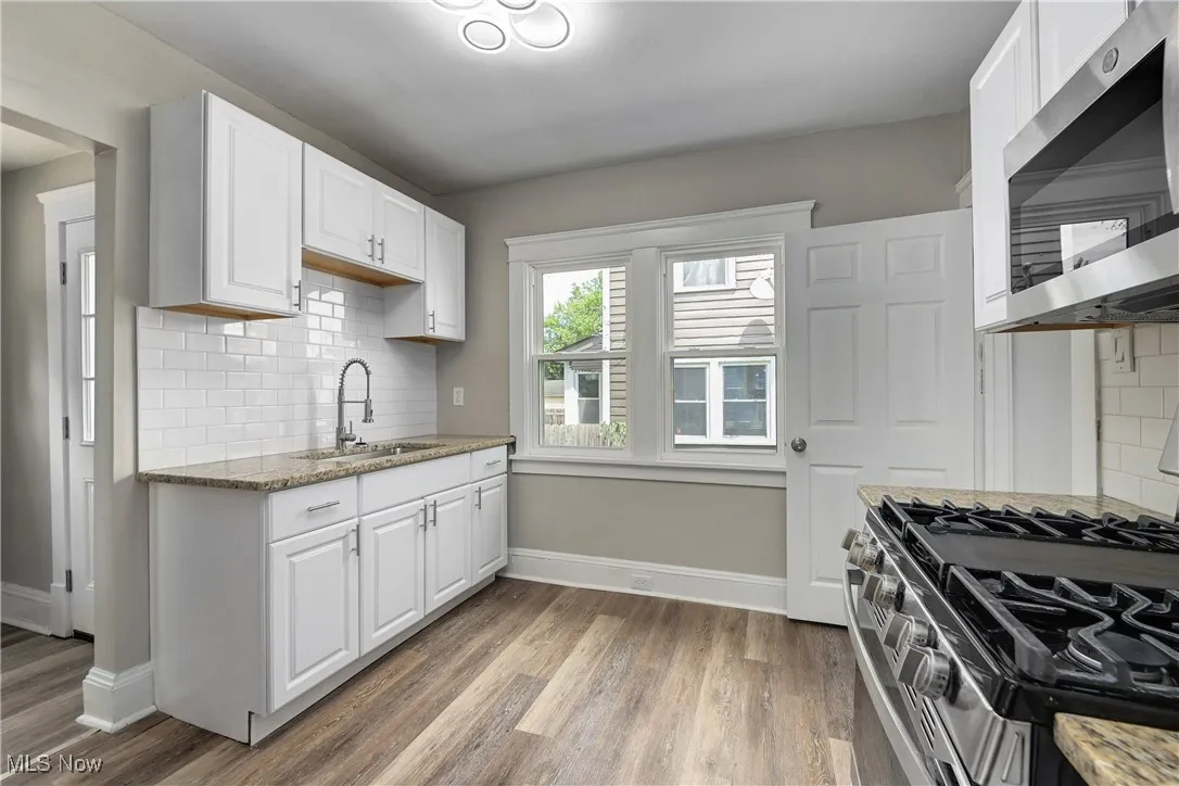 Kitchen featuring appliances with stainless steel finishes, decorative backsplash, light wood-type flooring, light stone counters, and white cabinetry