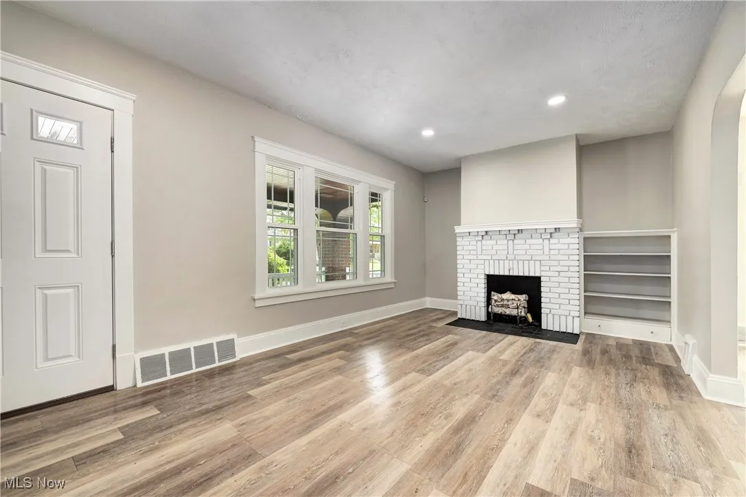 Unfurnished living room featuring wood finished floors, recessed lighting, and a brick fireplace