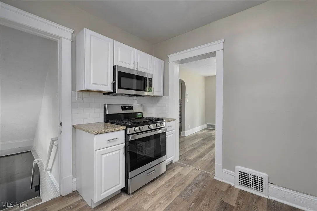 Kitchen with stainless steel appliances, light wood-style floors, white cabinetry, backsplash, and arched walkways