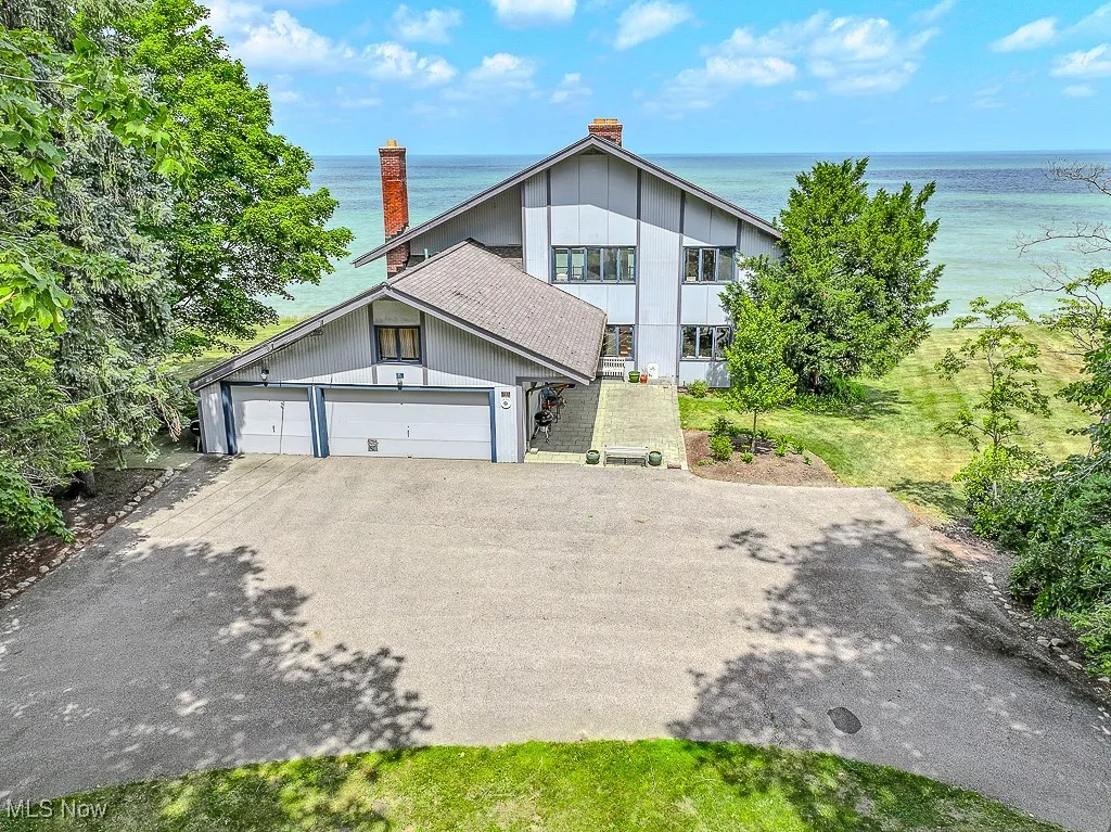 View of front facade with asphalt driveway, a water view, a chimney, and an attached garage