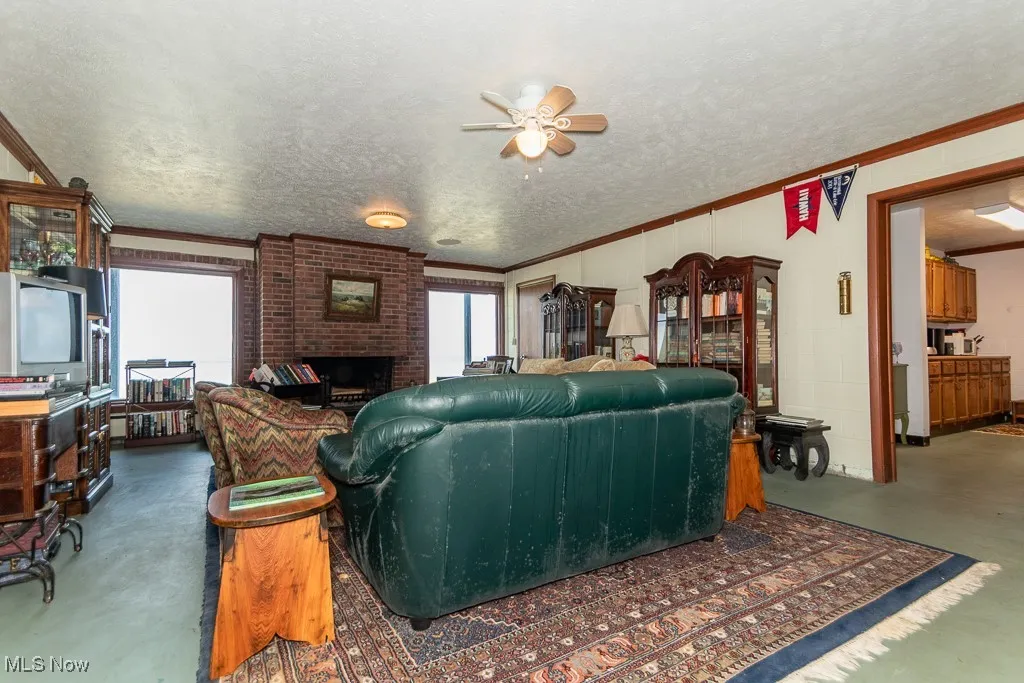Living room with ceiling fan, ornamental molding, a brick fireplace, and a textured ceiling